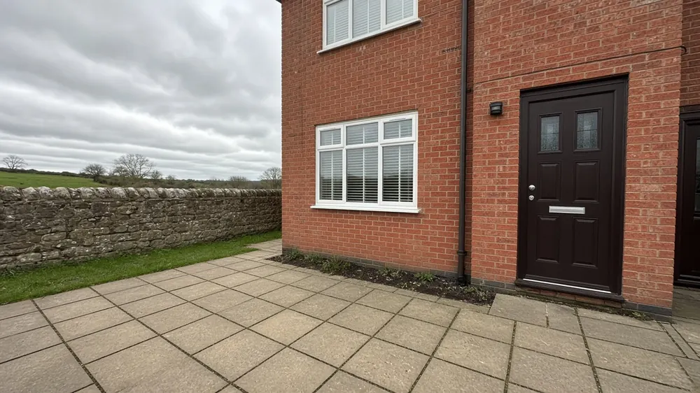 Example image: buff slab patio with a low stone wall behind a brick semi-detached house in a coastal village