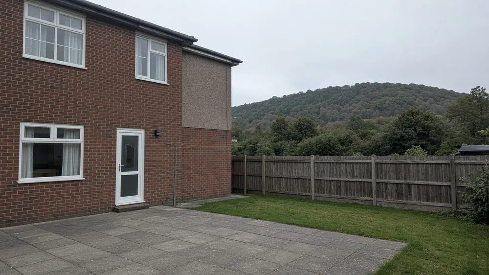 Example image: grey concrete slab patio behind a red brick semi-detached house with hills beyond